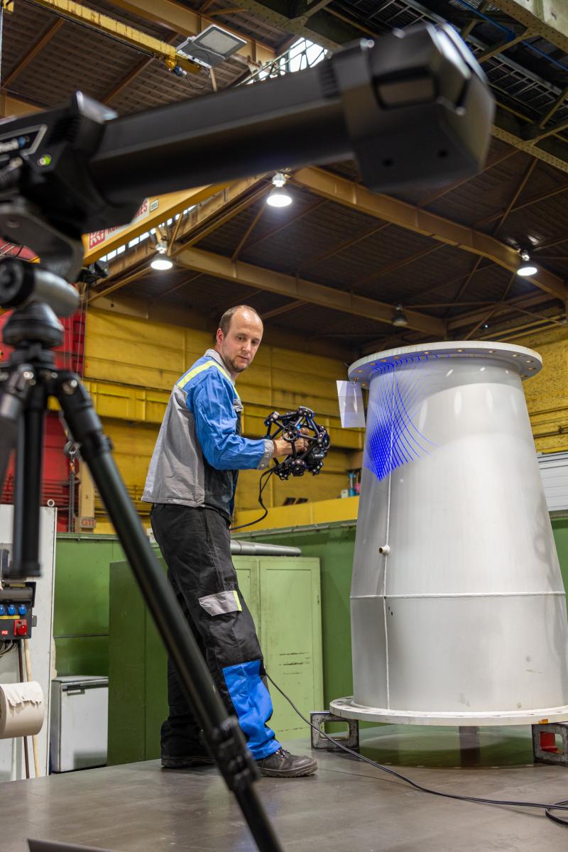 男子用 MetraSCAN 3D 扫描高炉的一段管道。前景是架在三脚架上的 C-Track 光学追踪器。