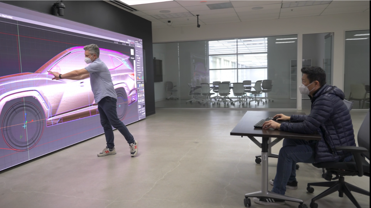 员工在一个大屏幕前,在坐在办公桌旁的同事面前展示汽车设计示意图